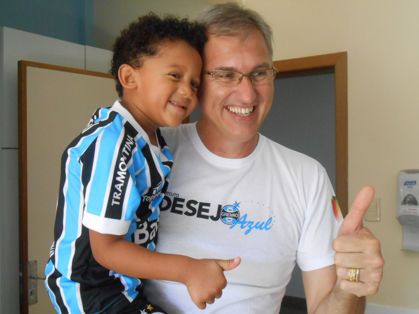 Hiago tem 6 anos e faz tratamento de saúde no Instituto de Cardiologia. Esbanja simpatia e alegria. Um rico de um guri Tricolor. Queria muito ganhar o uniforme completo do seu time do coração. E nada melhor para homenagear esse menino do que um ilustre voluntário como o campeão olímpico de vôlei Paulão. Os gremistas Hiago e Paulão fizeram um dobradinha de sucesso. Grande sacada Paulão! Força Hiago! 