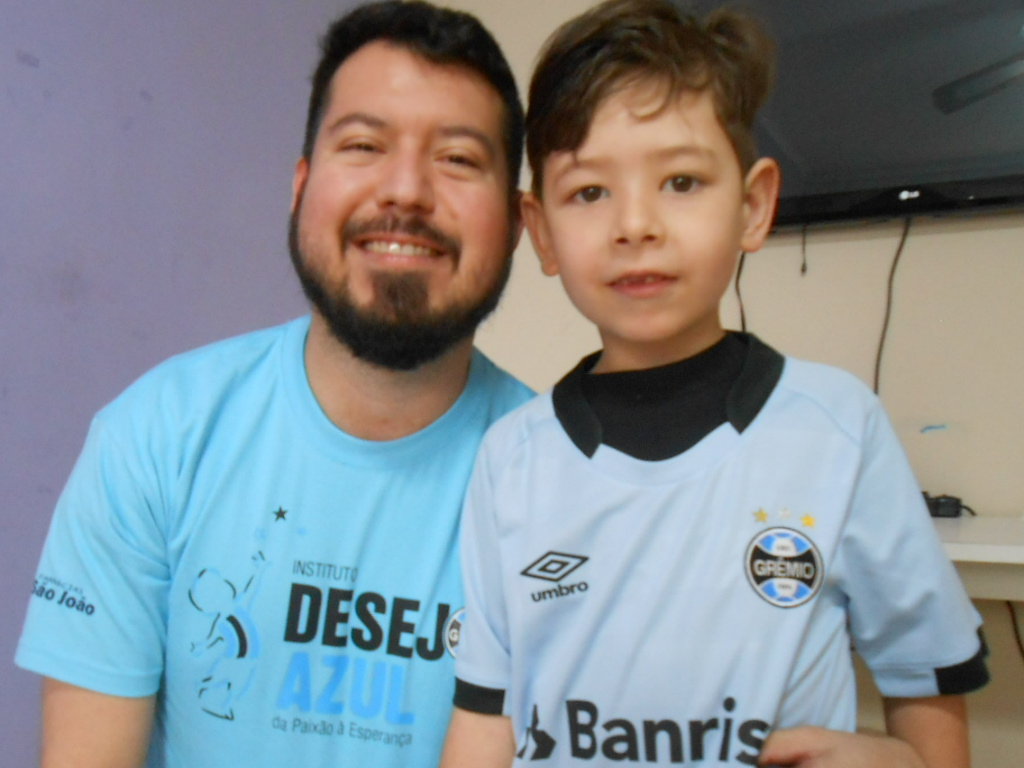 Luis Gustavo faz tratamento na APAE de Canoas. Estava empolgadíssimo com o presente que estava prestes a receber. E quando o voluntário Lucas Fernandes lhe entregou o pacote Gustavo não teve dúvidas e abriu com vontade e de pronto vestiu com orgulho a camiseta celestes tricolor.