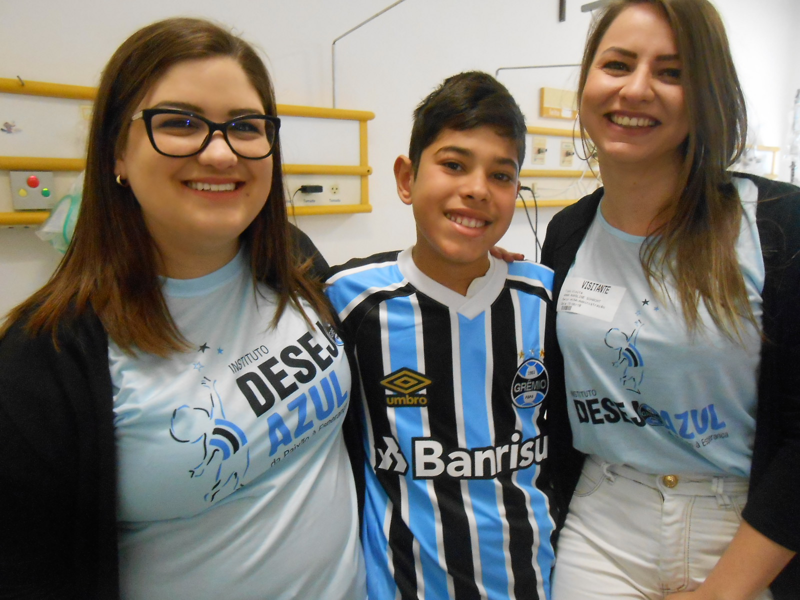 Kaiã está começando seu tratamento no Hospital da Criança Santo Antônio. Estava eufórico e emocionado com o presente que estava prestes a ganhar das voluntária Letícia Kessler e Anna Schachtl. Uma camiseta oficial do Grêmio para dar mais força no seu tratamento.